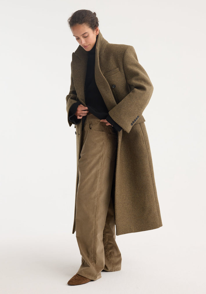 Hourglass wool coat in forest melange on model; features double-breasted design, strong shoulders, feminine waist, styled over a black sweater and tan trousers.