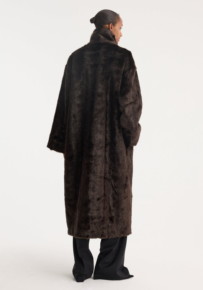 Model wearing a Mandarin faux fur coat in dark brown, featuring mandarin closures and stand-up collar, with black trousers, viewed from the back.