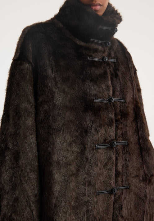 Model wears a Mandarin faux fur coat in dark brown, featuring toggle closures and a stand-up collar, paired with wide-leg black trousers, exuding a chic, sophisticated look.