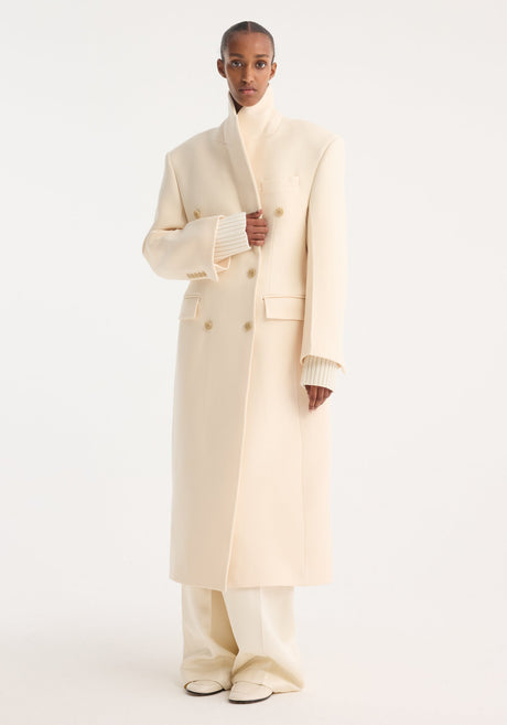 Model wearing Hourglass wool coat, off white, featuring a double-breasted design and strong shoulders, paired with matching trousers and loafers for a minimalist look.
