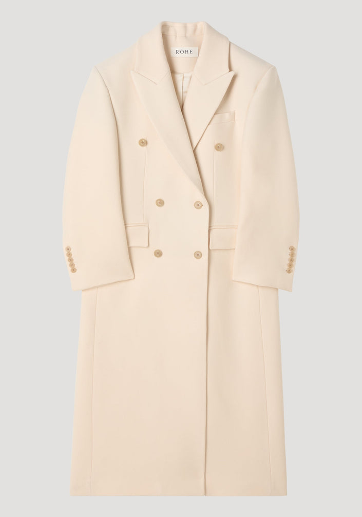 Hourglass wool coat in off white with double-breasted design, peaked lapels, hip flap pockets, and a full-length skirt, showcasing a feminine, structured silhouette.