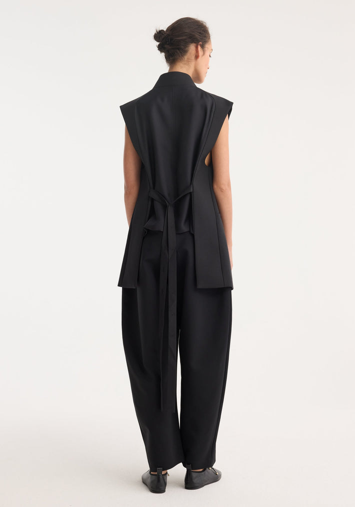 Reimagined oversized gilet in black, featuring extended shoulder panels, long tie-straps, and a silk back insert, worn with wide-leg trousers.