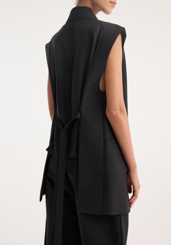 Back view of a woman in a Reimagined oversized gilet, showcasing a tailored black vest with a silk back and adjustable draping belt.