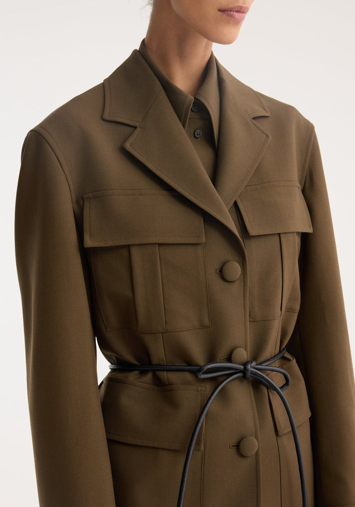 Safari blazer-jacket in virgin wool, featuring a notched lapel, oversized flap pockets, three buttons, and a black cord belt. Tailored yet relaxed fit.