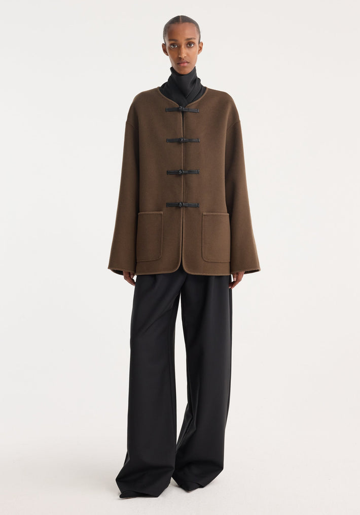 Model in Mandarin double-faced wool jacket | taupe, featuring black toggle closures, patch pockets, with embroidered edges, styled over a high-neck top and wide-leg trousers.