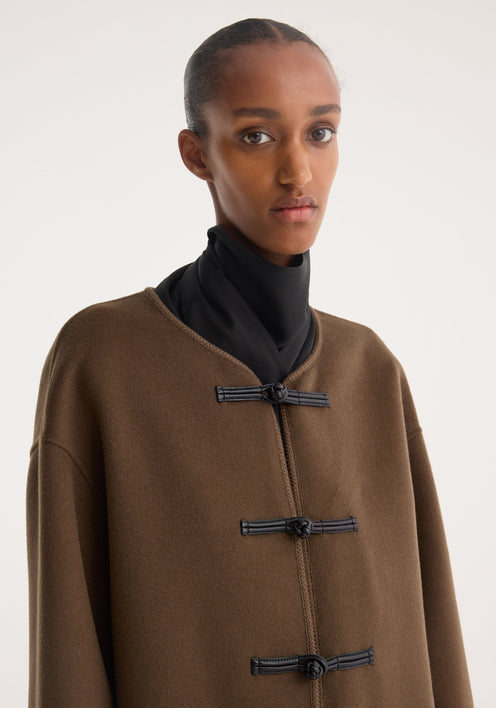 Model in Mandarin double-faced wool jacket | taupe, featuring black toggle closures, patch pockets, with embroidered edges, styled over a high-neck top and wide-leg trousers.