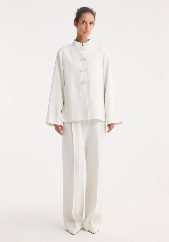 Person wearing a minimalist Mandarin jacket 'Marie' in winter white, featuring wide sleeves, pankou closures, and patch pockets, paired with matching wide-leg trousers.