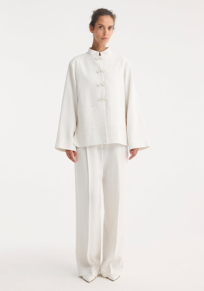 Person wearing a minimalist Mandarin jacket 'Marie' in winter white, featuring wide sleeves, pankou closures, and patch pockets, paired with matching wide-leg trousers.