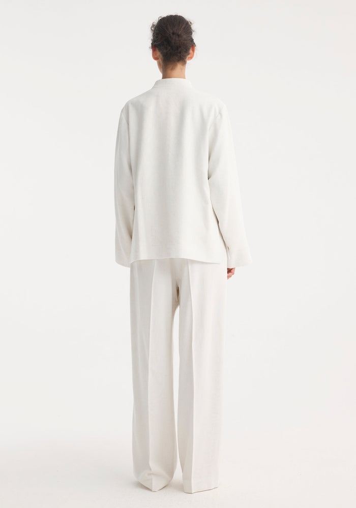 Model wearing Mandarin jacket in winter white, featuring wide sleeves, pankou closures, and patch pockets, paired with high-waisted, wide-leg trousers.