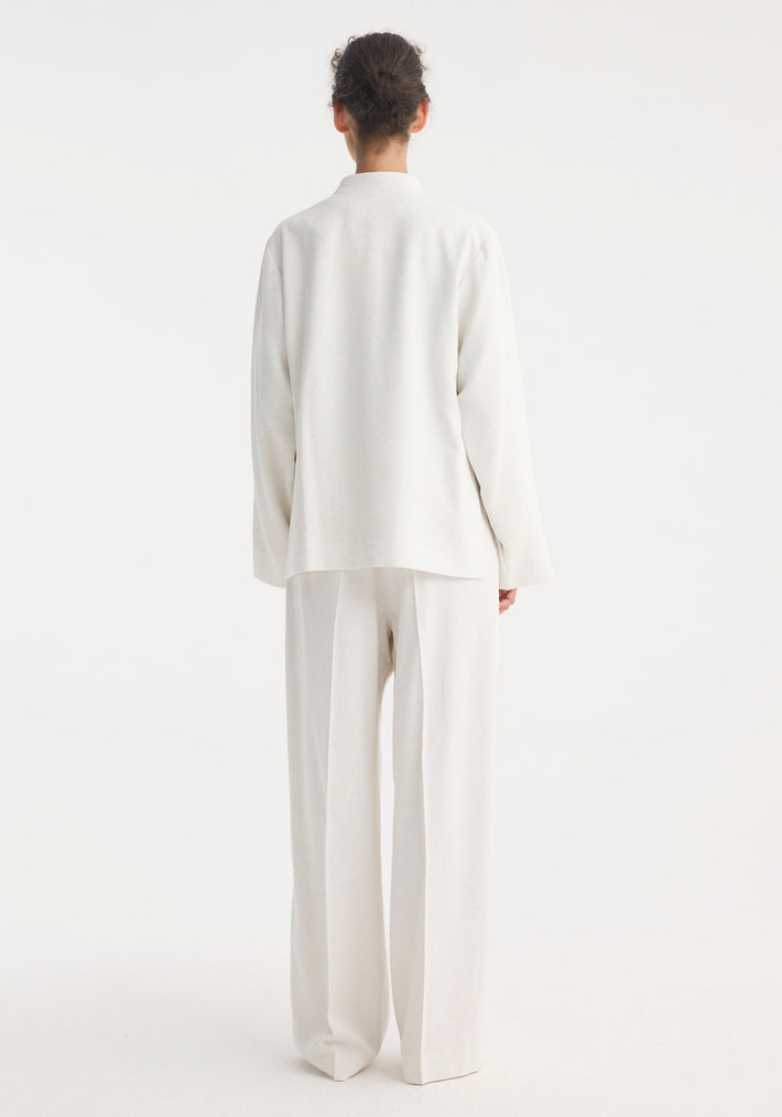 Model wearing Mandarin jacket in winter white, featuring wide sleeves, pankou closures, and patch pockets, paired with high-waisted, wide-leg trousers.