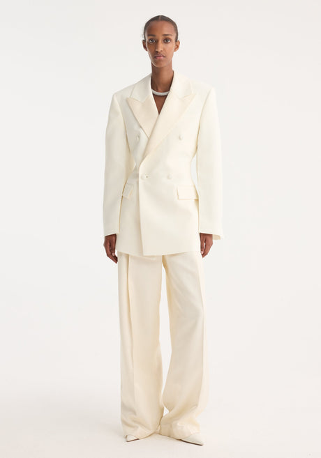 Model wearing Hourglass tuxedo blazer with sharp notch lapel, defined shoulders, cinched waist, and matching wide-leg trousers, emphasizing a structured, feminine silhouette.