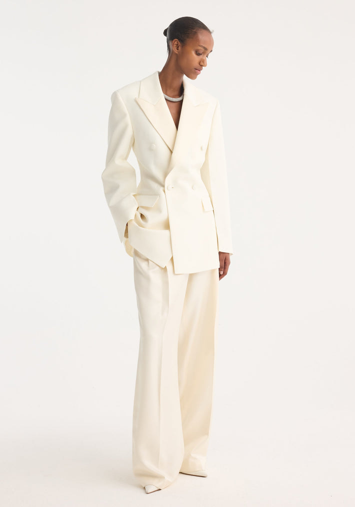 Model in an Hourglass tuxedo blazer, off white, featuring a sharp notch lapel, strong shoulders, cinched waist, paired with wide-leg trousers.