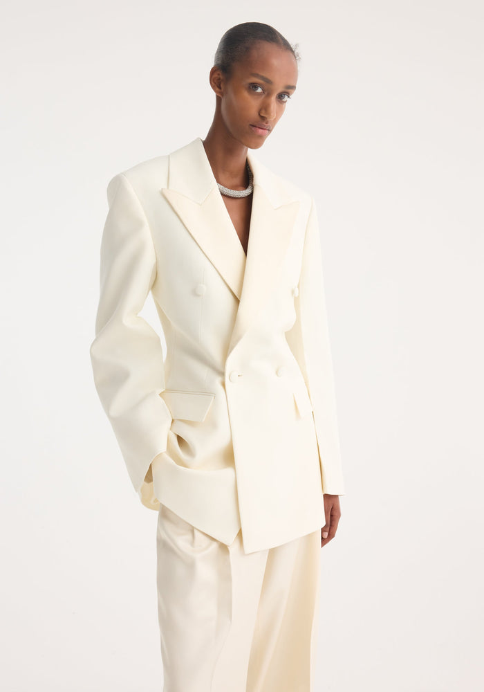 Model wearing Hourglass tuxedo blazer | off white, featuring a sharp notch lapel, padded shoulders, and cinched waist, paired with matching wide-leg trousers.