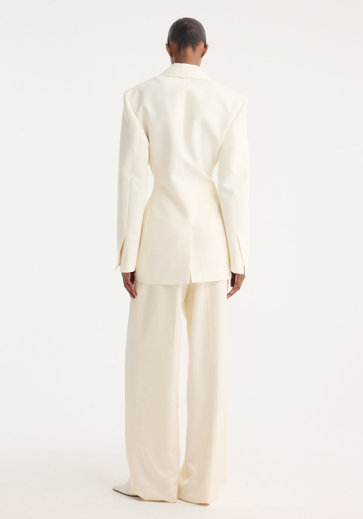 Back view of a model in an off-white Hourglass tuxedo blazer, showcasing sharp notch lapel, strong shoulders, and cinched waist paired with wide-leg trousers.