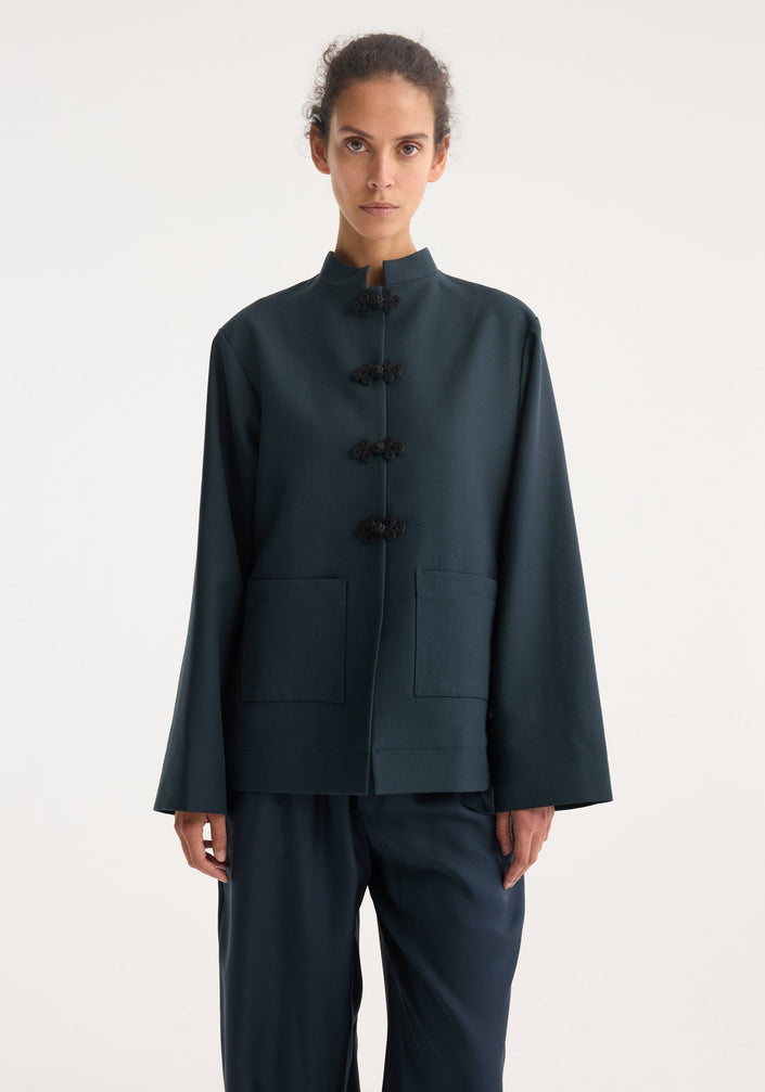 Model in Mandarin jacket | storm featuring a boxy design with frog button closures and patch pockets, paired with wide-leg trousers and black flats.