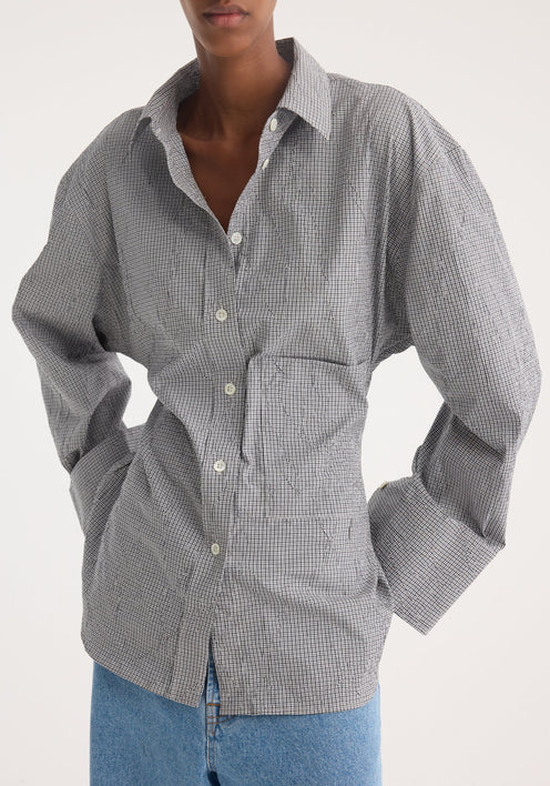 Model in a crushed checked shaped shirt with mini grey check, untucked, oversized sleeves, paired with wide-leg jeans and pointed-toe shoes, showcasing casual elegance.