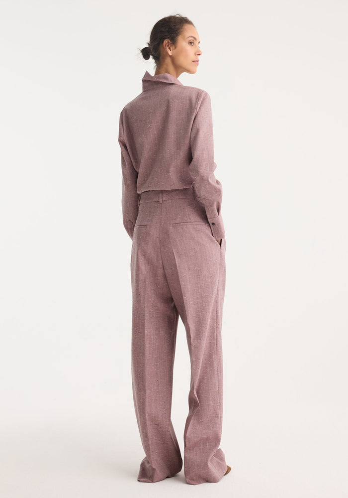 Woman in a fitted tweed shirt, mauve melange, showing a three-quarter profile with hands in pockets, highlighting the garment's sharp collar and refined silhouette.