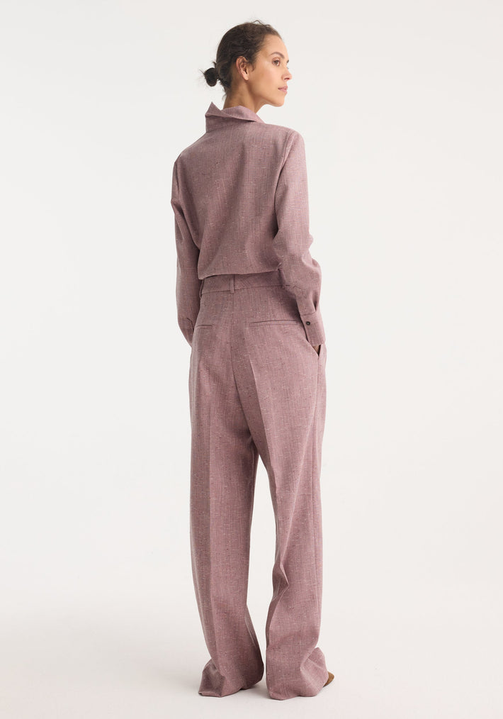 Woman in a fitted tweed shirt, mauve melange, showing a three-quarter profile with hands in pockets, highlighting the garment's sharp collar and refined silhouette.