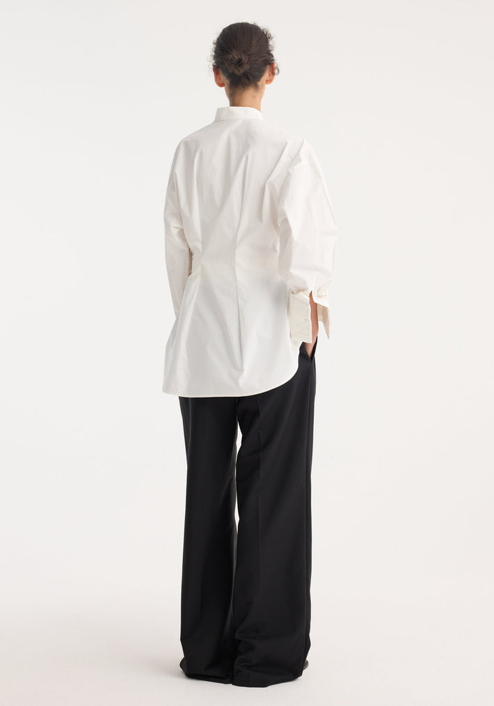 Person wearing the Tuxedo Wired Shaped Shirt with drop shoulders, stand collar, and statement cuffs, paired with wide-leg trousers, viewed from the back.