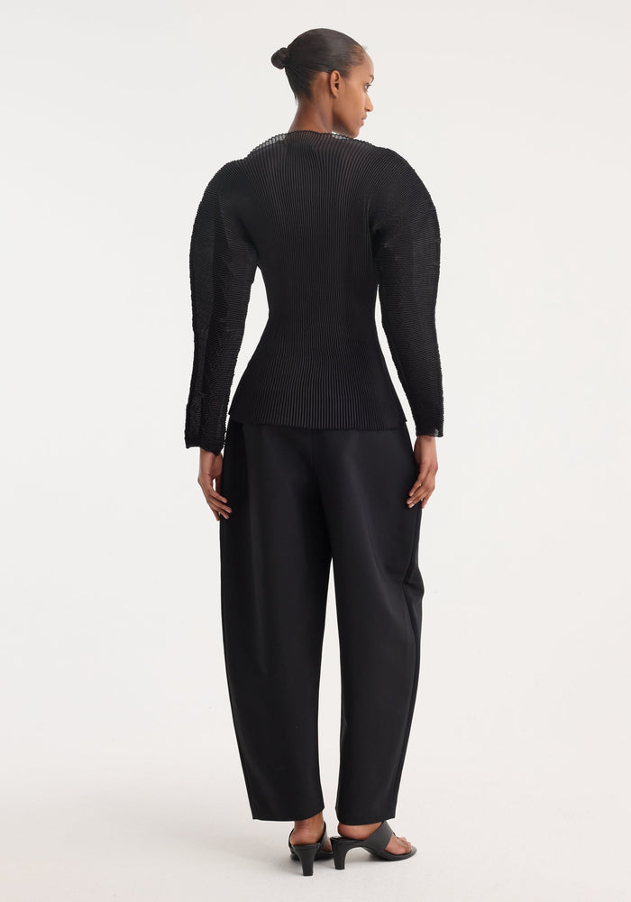 Model wearing Sculptural plissé top | black, featuring voluminous, pleated sleeves and a flared waist, paired with high-waisted trousers and open-toe heeled sandals.