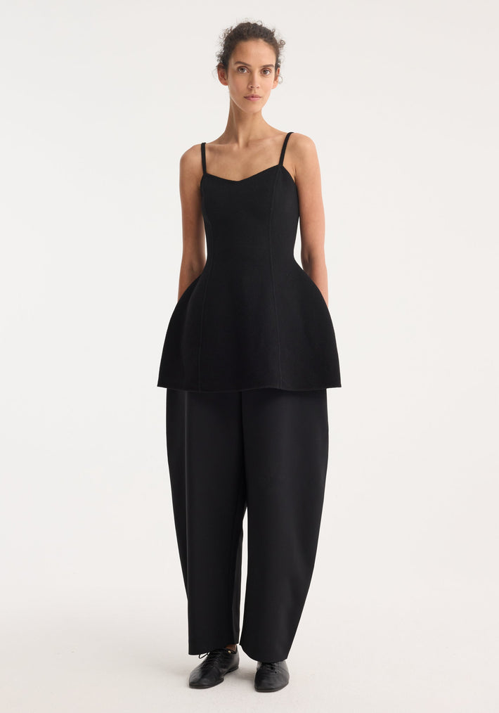 Model wearing Bustier double-faced top in black, featuring a fitted silhouette with thin straps and a flared peplum hem, paired with wide-leg trousers.