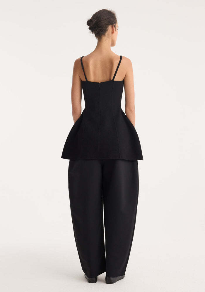 Woman in a black bustier double-faced top with peplum waist, spaghetti straps, and wide-leg trousers, showcasing an elegant, structured silhouette.
