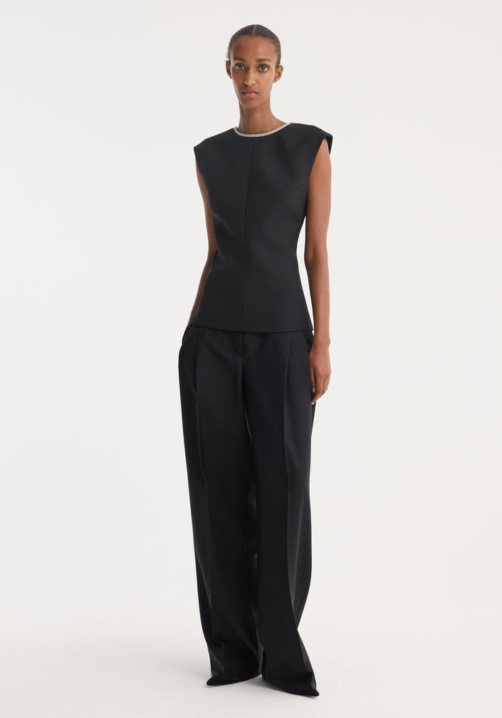 Model in sleeveless, form-fitting Open back appliqué top | black, showcasing crystal detailing on open back, paired with high-waisted, wide-leg trousers against a plain background.