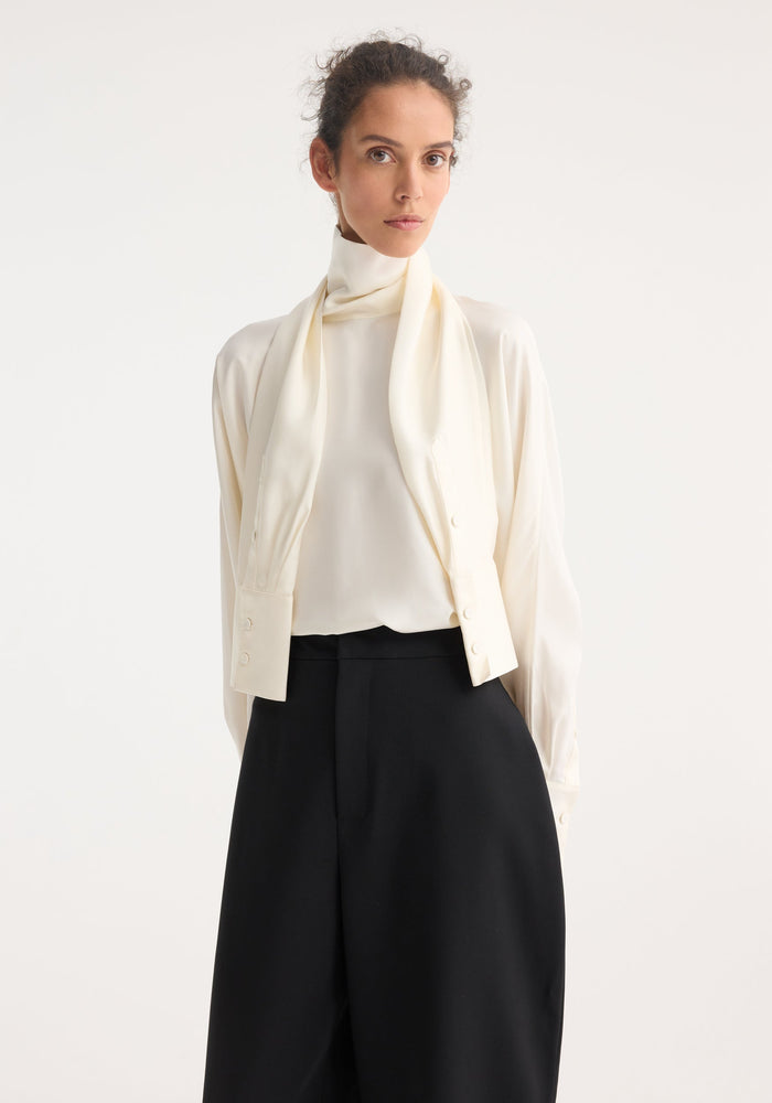 Model wearing Foulard silk top with draped sleeves, showcasing its soft, fluid silhouette, paired with high-waisted black trousers and styled with a simple updo.