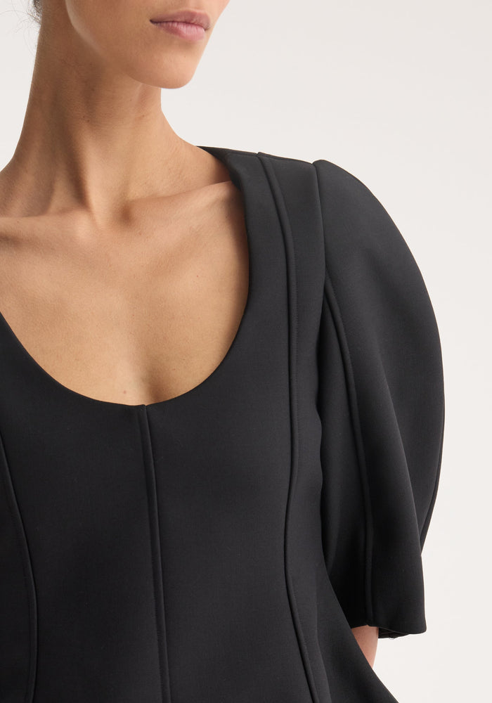 Woman wearing Sculptural top | black with a scooped neckline, softly puffed short sleeves, and visible seam detailing, showcasing a structured peplum silhouette.