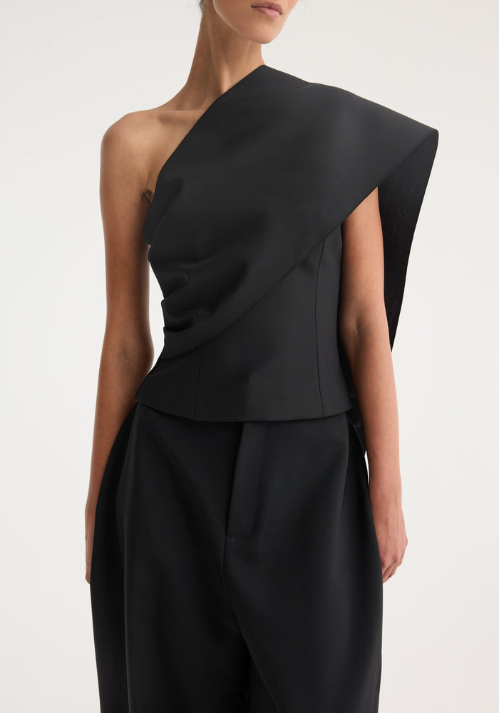 Model wearing a One-shoulder cape top | black, featuring an asymmetrical draped sash over the shoulder, paired with matching wide-leg trousers, showcasing elegant evening attire.