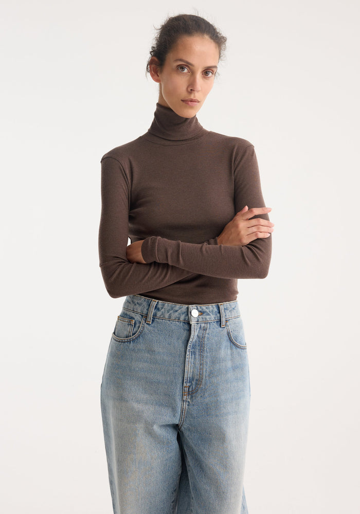 Person wearing Fine merino turtleneck in brown melange, featuring a fitted silhouette with long sleeves, paired with high-waisted light-wash blue jeans.