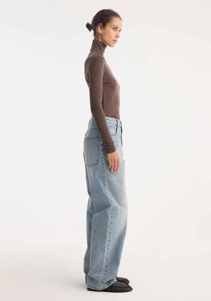 Model in fitted Fine merino turtleneck, brown melange, paired with high-waisted wide-leg jeans and black loafers, highlighting the turtleneck's 100% wool composition.