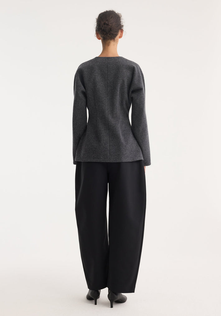 Person wearing Mandarin waisted cardigan with leather closures, showcasing its tailored structure and cinched waist, paired with wide-leg trousers and heeled shoes.