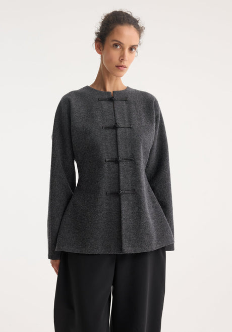 Model wears Mandarin waisted cardigan in mid grey melange, featuring long sleeves, round neckline, and leather pankou closures, paired with high-waisted trousers and ankle boots.