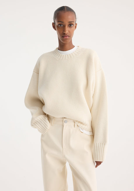 Model wears Sculptural compact crewneck in off-white, showcasing its oversized, relaxed fit with drop shoulders, paired with matching wide-leg trousers and slip-on shoes.