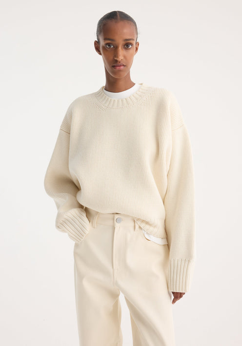 Model wears Sculptural compact crewneck in off-white, showcasing its oversized, relaxed fit with drop shoulders, paired with matching wide-leg trousers and slip-on shoes.