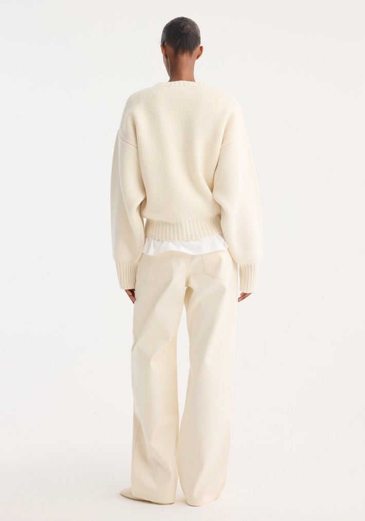 Person wearing an oversized Sculptural compact crewneck in off white, layered over a shirt, with wide-leg trousers, viewed from behind against a plain background.