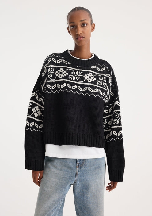 Model wearing a Fair-isle knitted jumper in black, featuring a boxy, cropped fit. Styled with light-wash wide-leg jeans and black pointed-toe shoes.