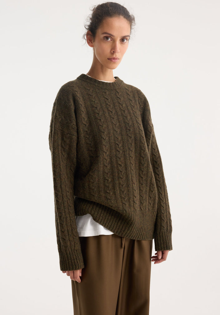 Model in oversized Cable knit jumper | forest melange, with a textured pattern and dropped shoulders, paired with wide-leg pants and loafers.