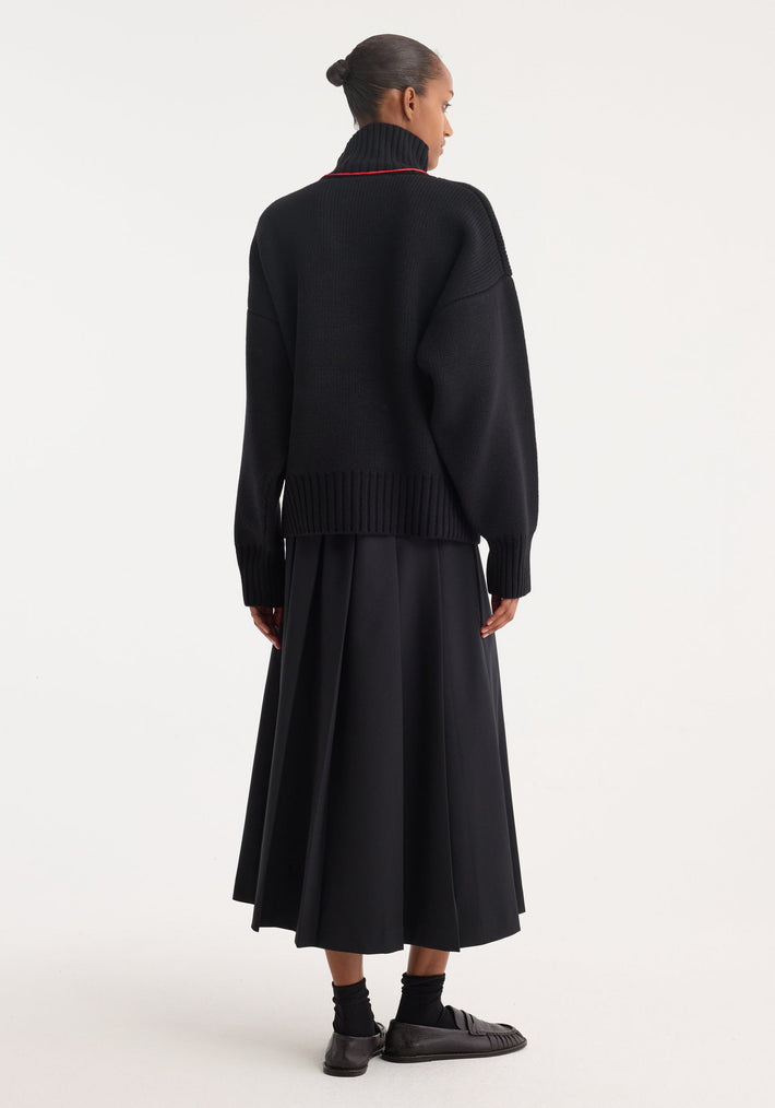 Model in a Sculptural compact turtleneck | black, showcasing its chunky knit, relaxed fit, and dropped shoulders, paired with a mid-calf A-line skirt.