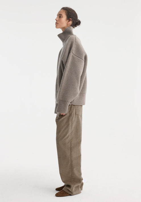Woman wearing Sculptural compact turtleneck | clay melange, an oversized grey knit with drop shoulders, over loose taupe trousers, styled with brown suede lace-up shoes.