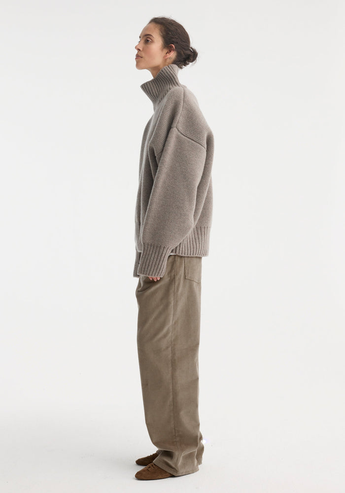 Person wearing the Sculptural compact turtleneck in clay melange, showcasing its relaxed fit and drop shoulder design, paired with beige corduroy-style trousers.