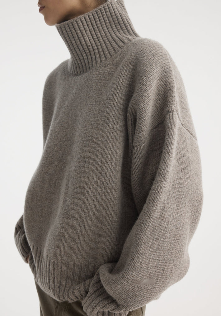 Sculptural compact turtleneck in clay melange, showcasing a high-neck, ribbed cuffs, and hem. Worn over corduroy trousers, highlighting its relaxed fit and volume.