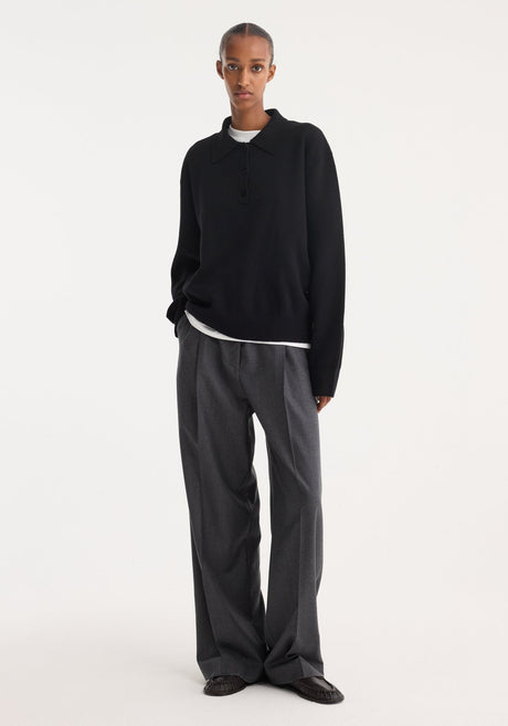 Tall person wearing a black Compact knitted polo with a three-button placket, over a white T-shirt, paired with wide-leg trousers and loafers.