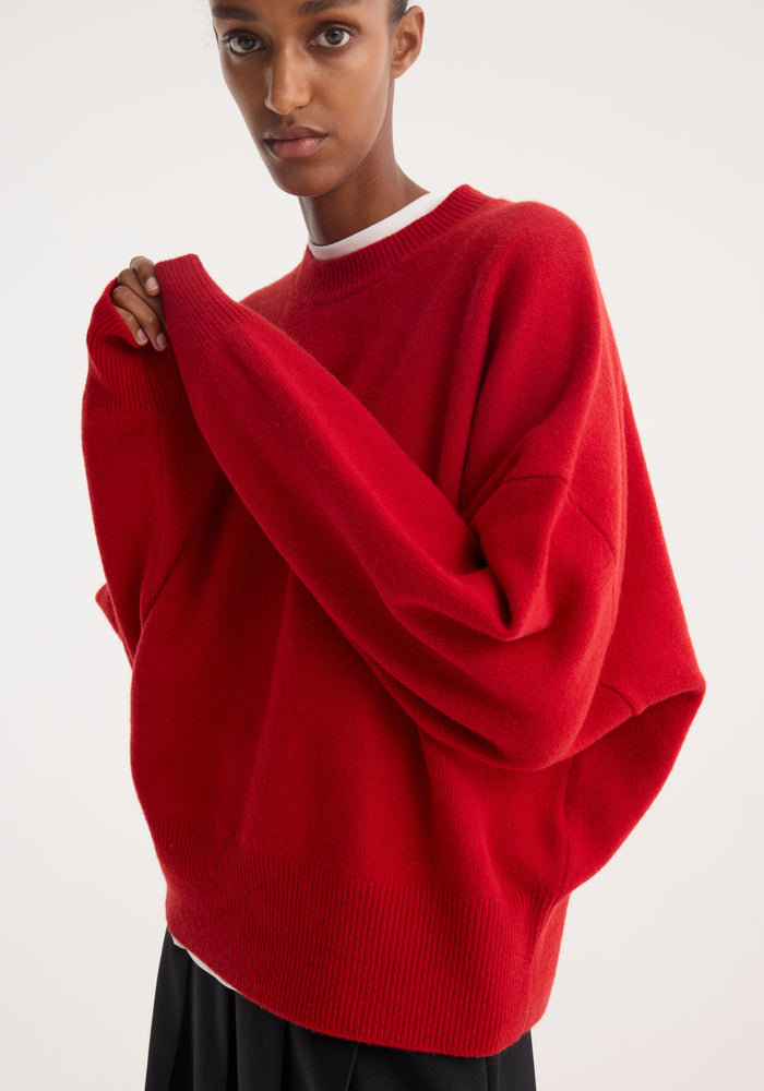 Boiled wool crewneck | rosso: Close-up of person in red knit sweater with ribbed neckline, dropped shoulders, balloon sleeves, and thick hem, holding sleeve edge.