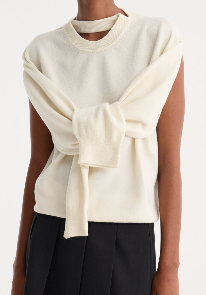 Person wearing an off-white Crewneck with open neck, featuring a sleeveless knit top and a draped long-sleeve sweater tied at the chest.