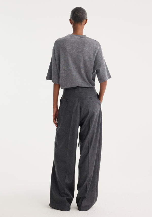 Person wearing Relaxed soft wool trousers | dark grey melange, featuring a wide-leg silhouette and drawstring waistband, crafted from lightweight virgin wool. Hair styled in a neat bun.