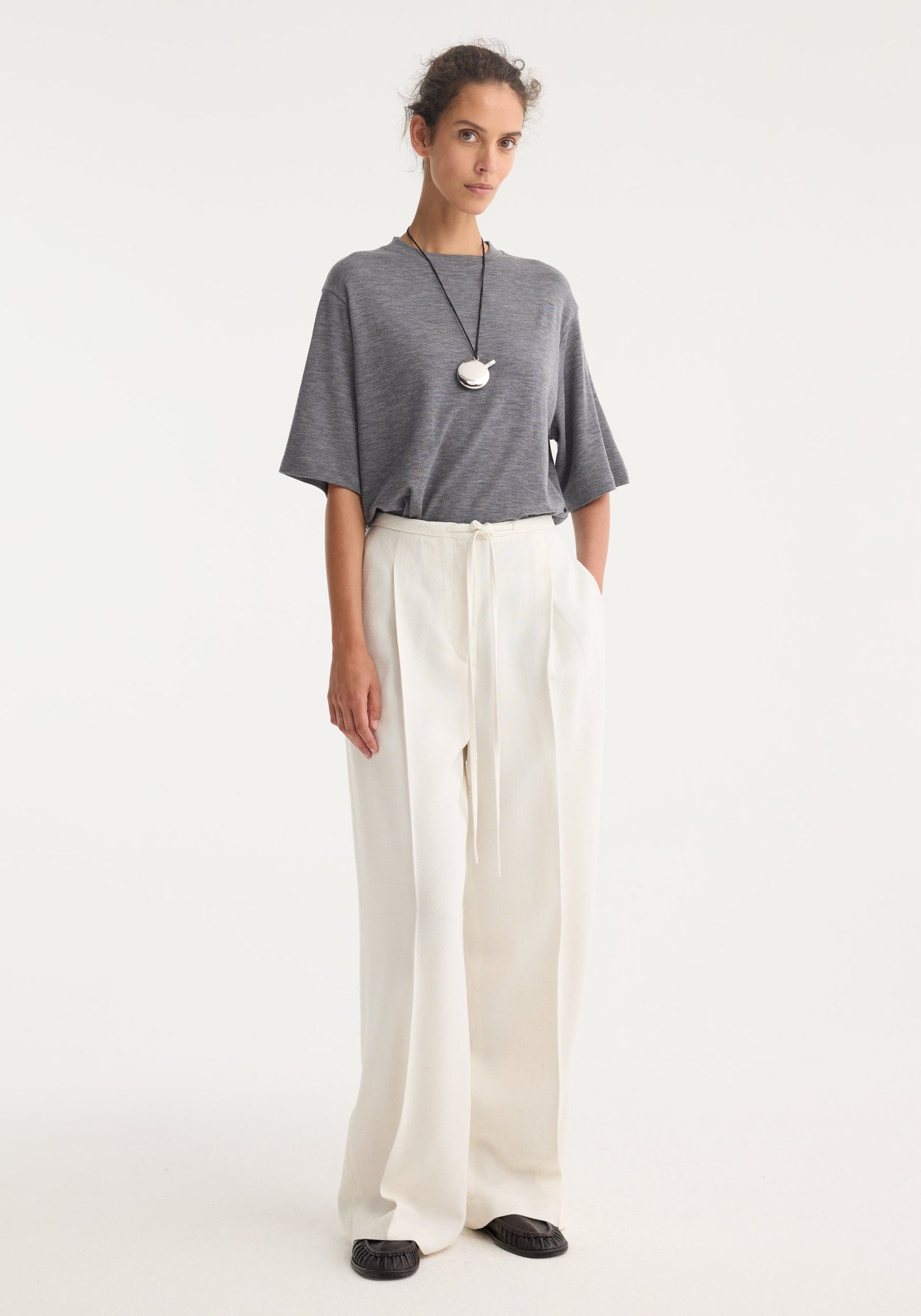 Model wears Relaxed drawstring trousers in winter white, showcasing a wide-leg, high-waisted design with a comfortable drawstring waistband, paired with a grey T-shirt.