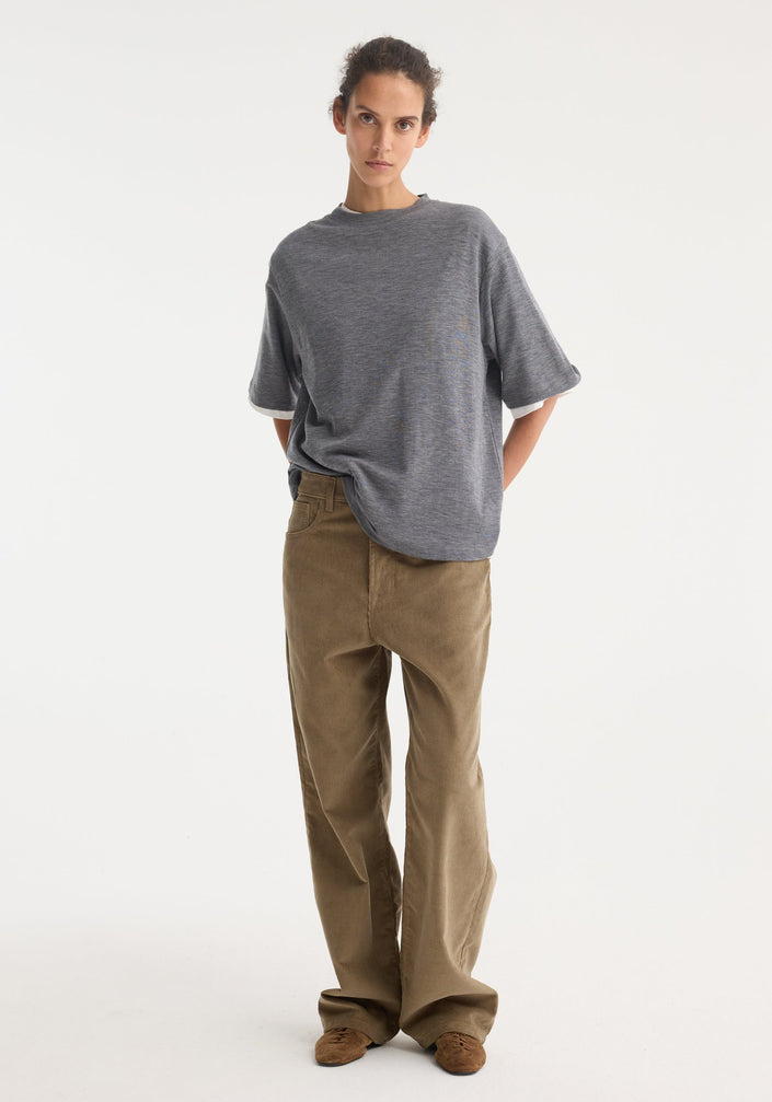 Relaxed corduroy trousers in dark sage, high-waisted with wide legs, paired with a heather-gray T-shirt. Styled with brown slip-on shoes.