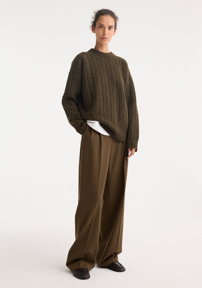Model wearing Signature tailored trousers in forest, showcasing a wide-leg, mid-waist fit with front pleats, paired with an oversized cable-knit sweater.